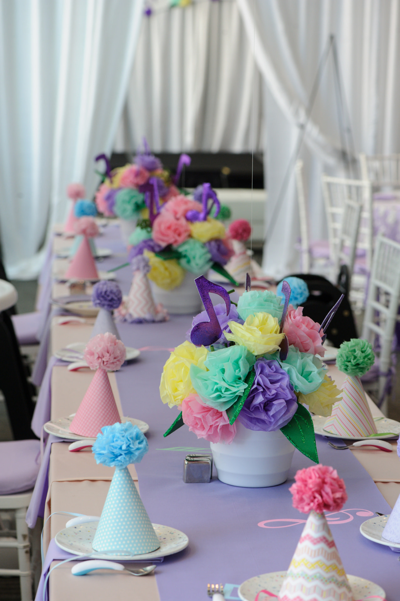 A long birthday table with pastel paper flowers, purple musical notes and handmade party hats