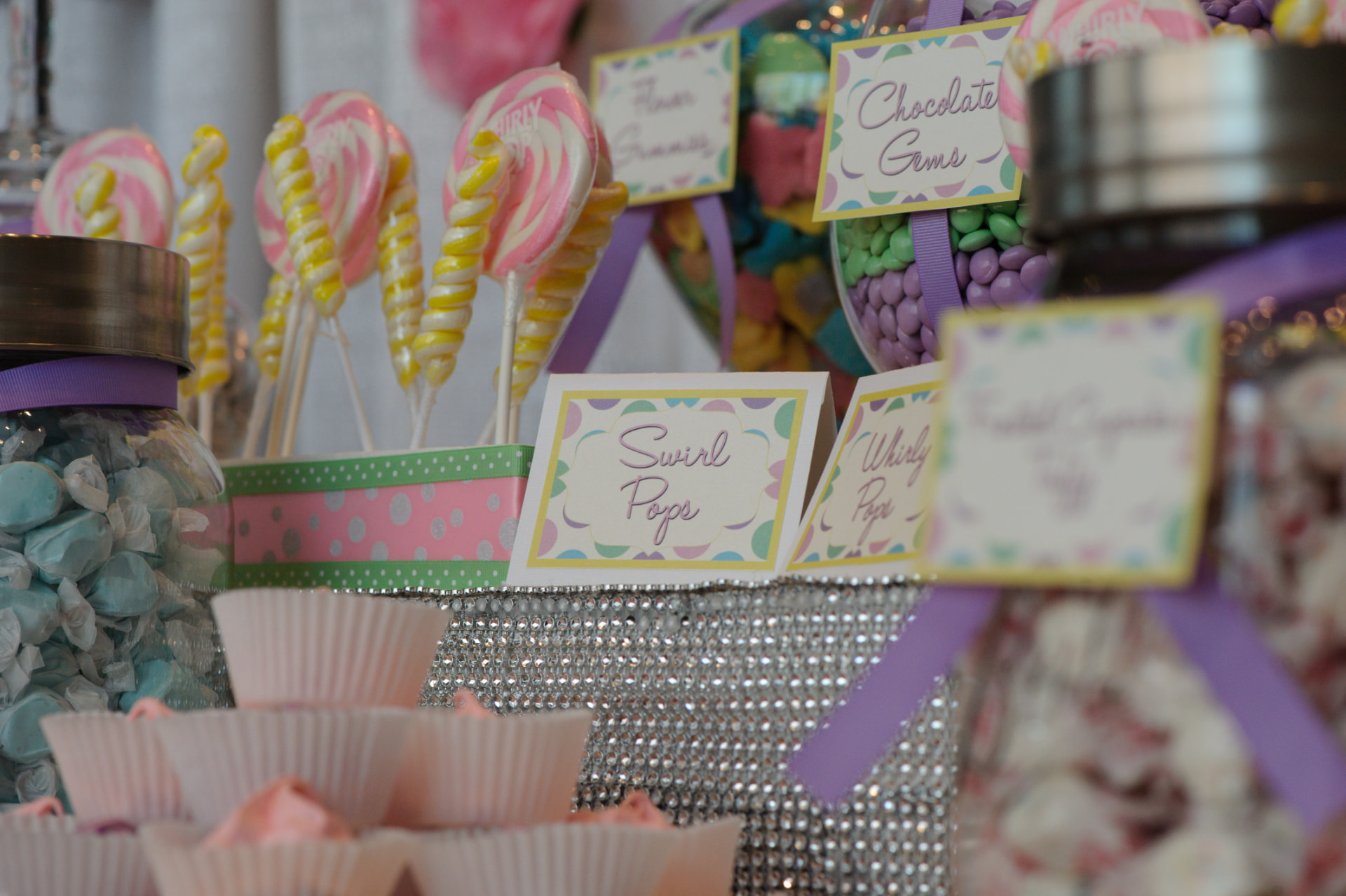 Pastel swirl lollipops and labeled candy jars on the birthday dessert table